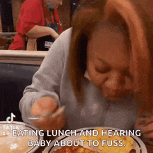 a woman is sitting at a table eating lunch and hearing baby about to fuss