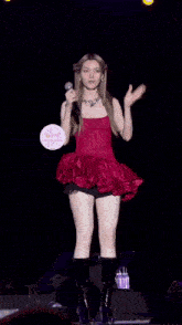 a woman in a red dress and black boots is singing into a microphone on stage .