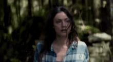 a woman in a plaid shirt is standing in a forest .