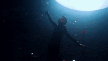 a man is standing in the dark with his arms outstretched in front of a large light