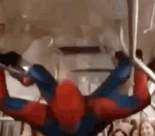 a man in a spiderman costume is hanging upside down from a rope .