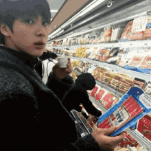 a man is standing in a grocery store holding a bag of ham