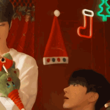 a man is holding a stuffed animal in front of a red wall with a santa hat hanging from it