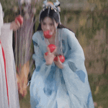 a woman in a blue dress is holding red apples