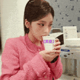 a woman in a pink jacket is drinking from a cup with the letter e on it