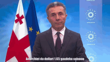 a man in a suit and tie stands in front of a flag and a sign that says www.co.de