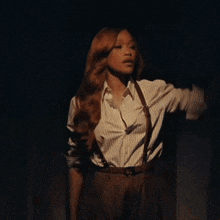 a woman in a striped shirt and suspenders is standing in a dark room