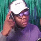 a man wearing glasses and a baseball cap is talking on a cell phone .