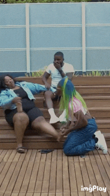 a group of people are sitting on a wooden bench and one of them is kneeling down to touch another person 's foot