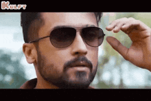 a man with a beard is wearing sunglasses and making a gesture with his hand .