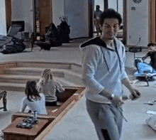 a man in a white hoodie is standing in a living room holding a skateboard .