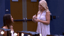a woman in a white dress talks to another woman in front of a door that says no smoking