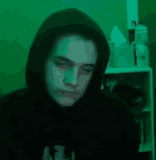 a man in a black hoodie is sitting in front of a green background .