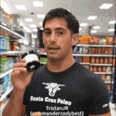 a man wearing a santa cruz paleo t-shirt holds a bottle
