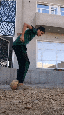 a boy in a green shirt is kicking a soccer ball in front of a building