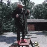 a man in a cowboy hat is standing on a wooden picnic table