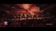 a man singing into a microphone while playing a guitar in front of a screen that says aer gu