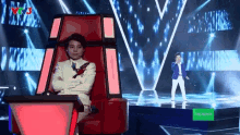 a boy in a suit is sitting in a chair on a stage with an oppo logo in the background