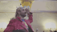 a man in a red jacket with spikes on it is waving his hand in front of a crowd .