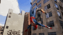 a man in a spiderman suit is upside down in front of a building with the word spiderman on it