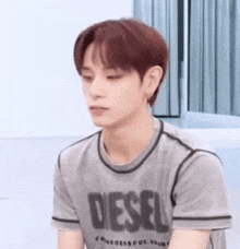 a young man with red hair is wearing a grey diesel t-shirt and looking down .