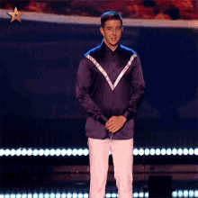 a man in a blue shirt and white pants stands on a stage with a star in the background