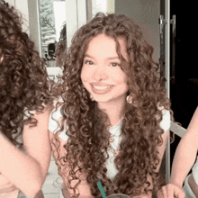 a woman with curly hair is smiling and looking at herself in the mirror