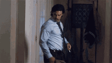 a man in a blue shirt and tie is smoking a cigarette while standing in a hallway .