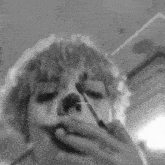 a black and white photo of a person smoking a cigarette and applying makeup to their face .