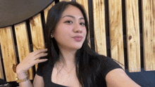 a woman wearing a black top and a gold necklace with the letter g on it