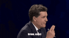 a man in a suit and tie says exact in front of a dark background