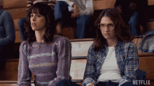 two women sit in a bleacher with a netflix logo on the bottom right