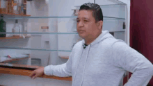 a man in a white hoodie is standing in front of a refrigerator in a kitchen .