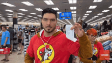 a man in a red shirt with a squirrel on it is holding up a receipt in a store