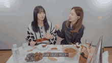 two girls are sitting at a table with a twice logo on the wall