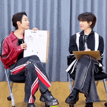 two men are sitting in chairs one is holding a piece of paper that says xlov on it