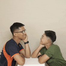 a boy wearing a green shirt that says army sits next to a man wearing glasses