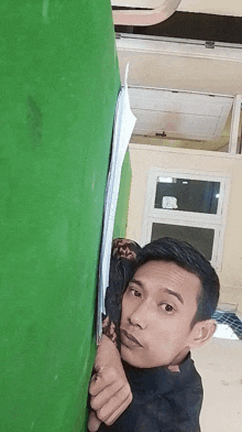 a man peeking behind a green wall with a piece of paper on it