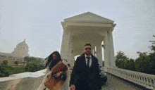 a man in a suit and tie is walking with a woman in front of a building