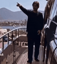 a man is standing on the deck of a boat pointing at something .