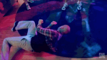 a man in a plaid shirt is laying on the floor in a room with purple lights .