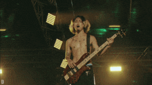 a man without a shirt is playing a bass guitar on stage