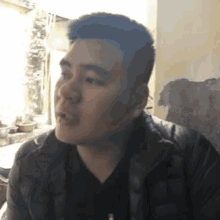 a man in a black jacket is making a funny face while sitting in front of a wall .