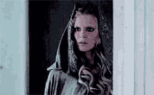 a woman is standing in a doorway wearing a hooded cape .