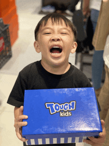a young boy is holding a blue tough kids shoe box