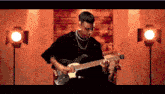 a young man is playing a guitar in a room with lights