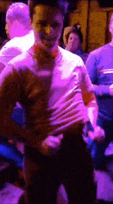 a man in a pink shirt is dancing in a dark room with purple lights .