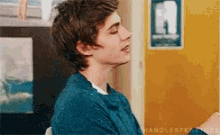 a young man wearing a blue sweater is sitting in front of a yellow door with a sign that says a on it
