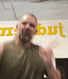 a man with a beard is standing in front of a wall with the word but written in yellow .