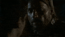 a man with a beard and long hair is looking at another man in the dark .